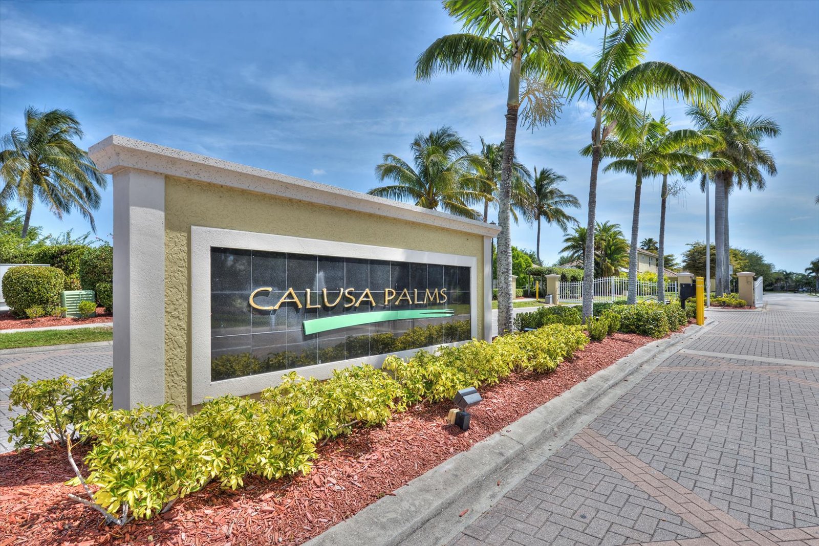The Calusa Palms entrance sign framed by tall palm trees under a bright blue Florida sky